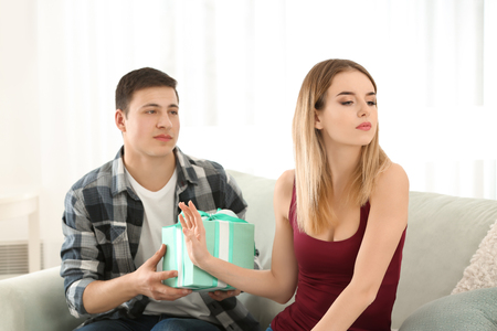Offended young woman refusing to take gift from her boyfriend at homeの写真素材