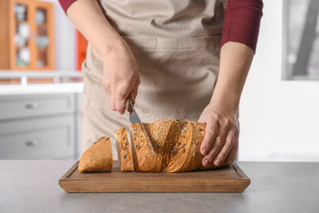 Woman cutting tasty bread on wooden boardの写真素材