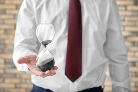 Man holding hourglass on blurred background, closeup. Time management conceptの写真素材