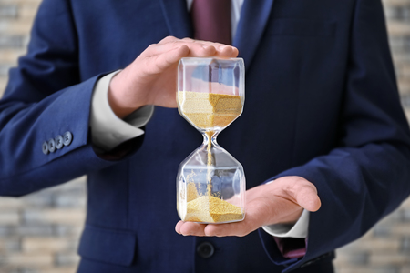Man holding hourglass on blurred background, closeup. Time management conceptの写真素材