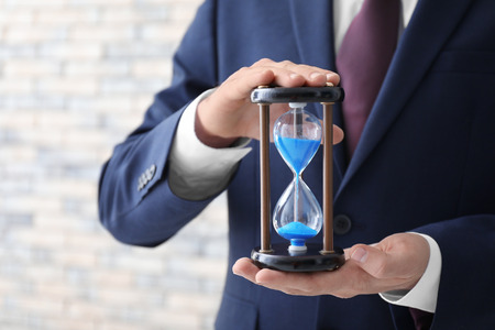 Man holding hourglass on blurred background, closeup. Time management concept