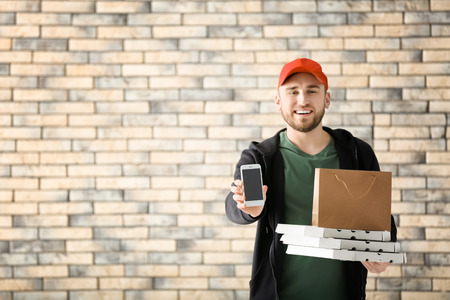 Young man with cardboard pizza boxes, paper bag and mobile phone on brick wall background. Food delivery serviceの写真素材