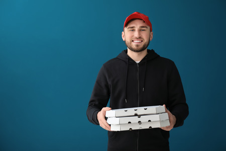 Young man with cardboard pizza boxes on color background. Food delivery serviceの写真素材
