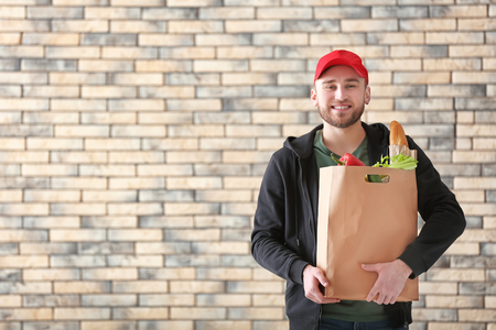 Young man with products in paper bag on brick wall background. Food delivery serviceの写真素材