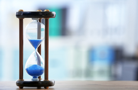 Hourglass on table against blurred background. Time management concept