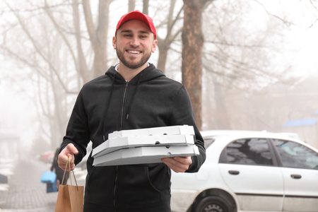 Young man with cardboard pizza boxes and paper bag outdoors. Food delivery serviceの写真素材