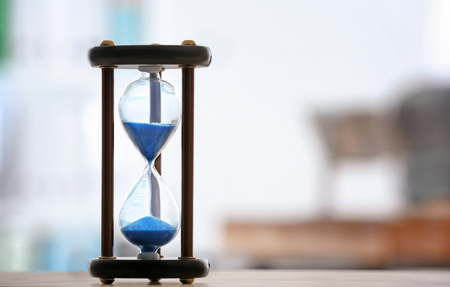 Hourglass on table against blurred background. Time management concept