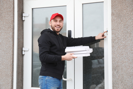 Young man with cardboard pizza boxes ringing doorbell outdoors. Food delivery serviceの写真素材