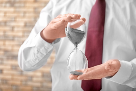 Man holding hourglass on blurred background, closeup. Time management concept
