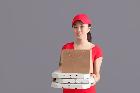 Asian woman with cardboard pizza boxes and paper bag on gray background. Food delivery serviceの写真素材
