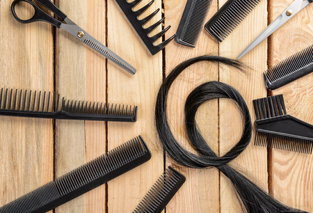 Flat lay composition with hairdresser's tools and strand of black hair on wooden backgroundの写真素材