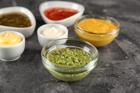 Bowls with different sauces on grey textured background
