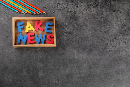 Phrase FAKE NEWS made with color letters in wooden box on gray backgroundの写真素材