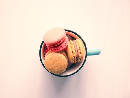Metal cup with tasty colorful macarons on white background