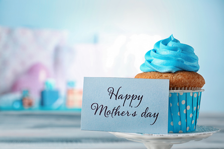 Tasty cupcake and card with words MOTHER'S DAY on table