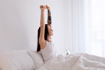 Young beautiful woman stretching on bed in morning