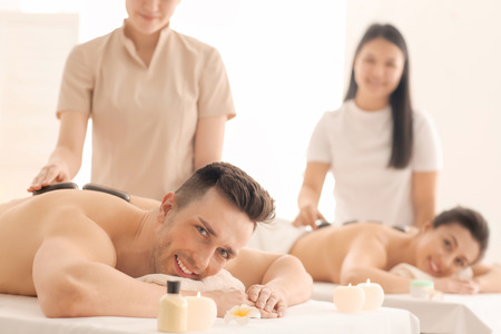 Happy young couple having stone massage in spa salonの写真素材