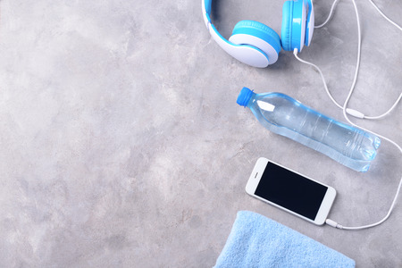 Flat lay composition with smartphone, bottle of water and headphones on grey background. Gym workout