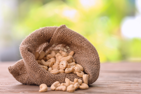 Sack with tasty cashew nuts on wooden table against blurred backgroundの写真素材