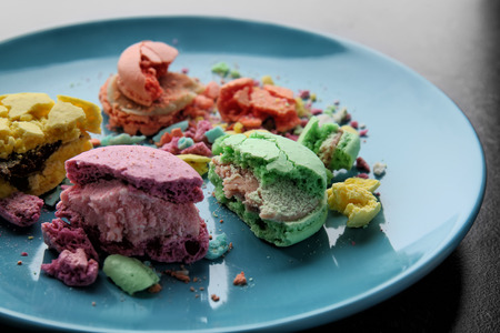 Plate with crushed macarons on dark background