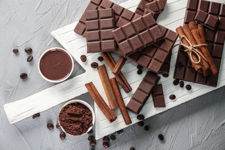 Flat lay composition with tasty chocolate, coffee beans and cinnamon sticks on wooden board