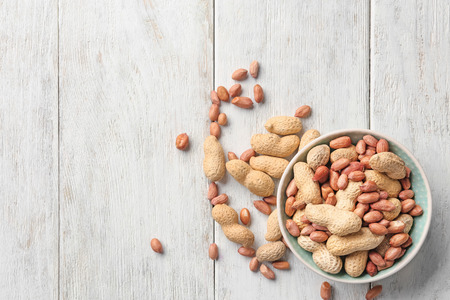 Bowl with peanuts on wooden background