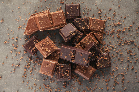 Pieces of dark and milk chocolate on gray background, top view