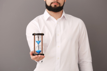 Man holding hourglass on gray background. Time management conceptの写真素材
