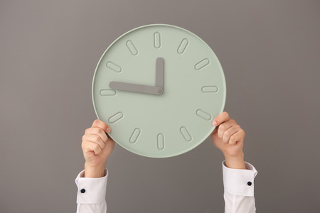 Man holding clock on gray background. Time management concept