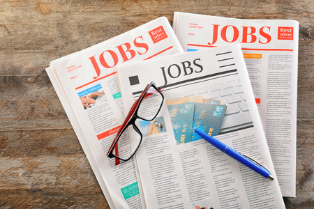 Newspapers with headlines JOBS and glasses on wooden background