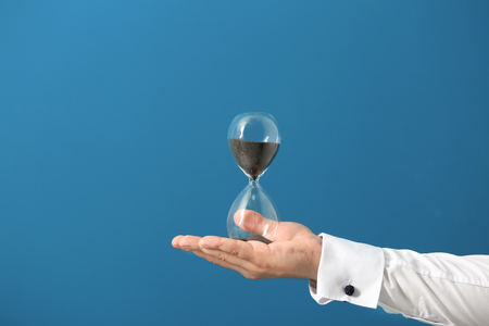 Man holding hourglass on color background. Time management concept