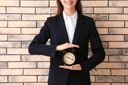 Woman holding alarm clock on brick background. Time management conceptの写真素材