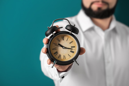 Man holding alarm clock on color background. Time management concept