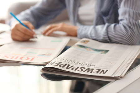 Young woman looking for job in newspapers indoorsの写真素材