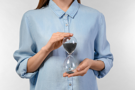 Woman holding hourglass on light background. Time management conceptの写真素材