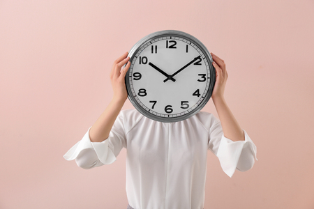 Woman hiding face behind clock on color background. Time management conceptの写真素材