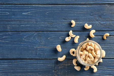 Tasty cashew nuts and glass jar on wooden background, top viewの写真素材