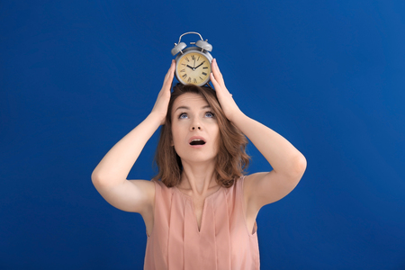Mature woman with alarm clock on head against color background. Time management conceptの写真素材
