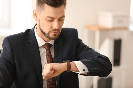 Businessman looking at his wristwatch in office. Time management conceptの写真素材