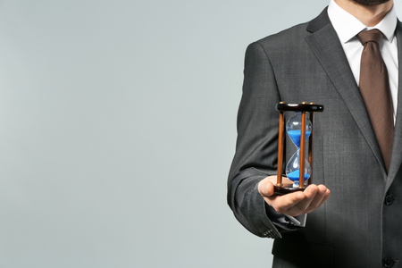 Man holding hourglass on grey background. Time management conceptの写真素材