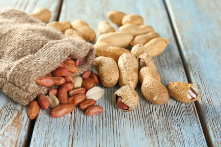 Tasty peanuts and sackcloth bag on wooden background