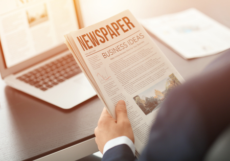 Handsome businessman reading financial newspaper in officeの写真素材