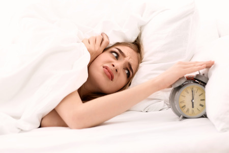 Young woman switching off alarm clock while lying in bed at homeの写真素材