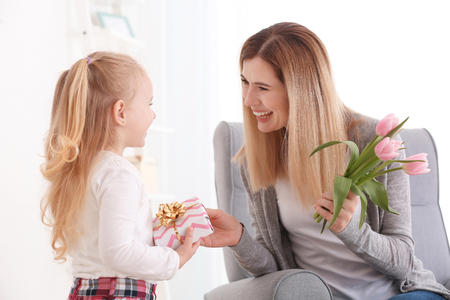 Mother receiving gift and flowers from her cute little daughter at homeの写真素材