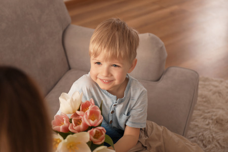 Cute little son giving flowers to his mother at home