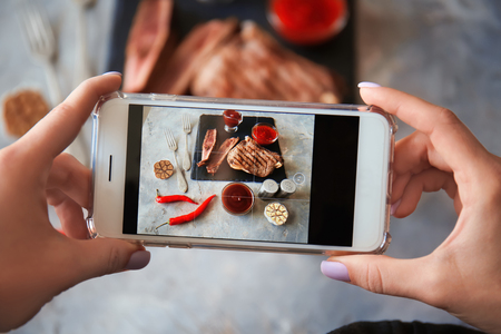 Woman taking photo of barbecue sauce and grilled meat with mobile phoneの写真素材