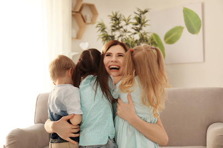 Smiling mother hugging her cute little children at homeの写真素材