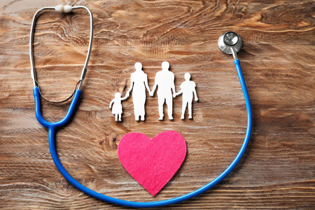 Family figure, heart and stethoscope on wooden background. Health care conceptの写真素材