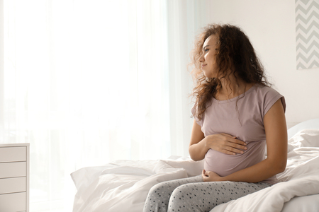 Morning of beautiful pregnant African-American woman in bedroomの写真素材