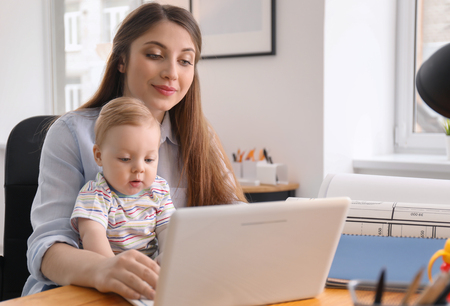 Young woman with baby working in officeの写真素材